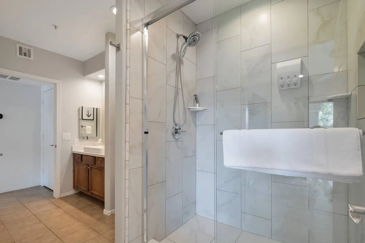 A bright, modern bathroom featuring a glass walk-in shower, elegant marble tiles, and a stylish vanity with a large mirror. The space exudes cleanliness and luxury, with ample light making the bathroom feel spacious and inviting.