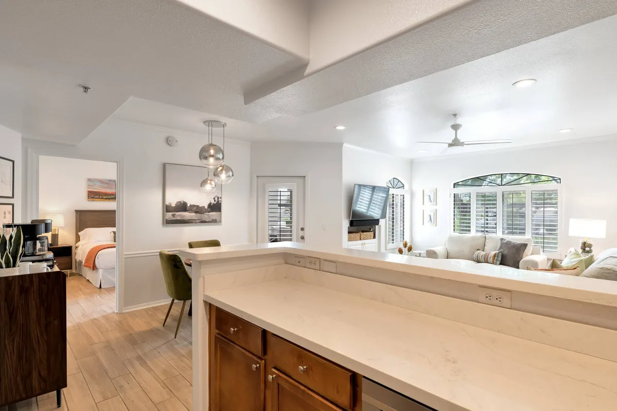 A broader perspective showing the open flow between the kitchen and living area, with large windows filling the space with light and providing a glimpse toward the patio. The arrangement invites both entertaining and relaxation, highlighting easy movement between spaces.