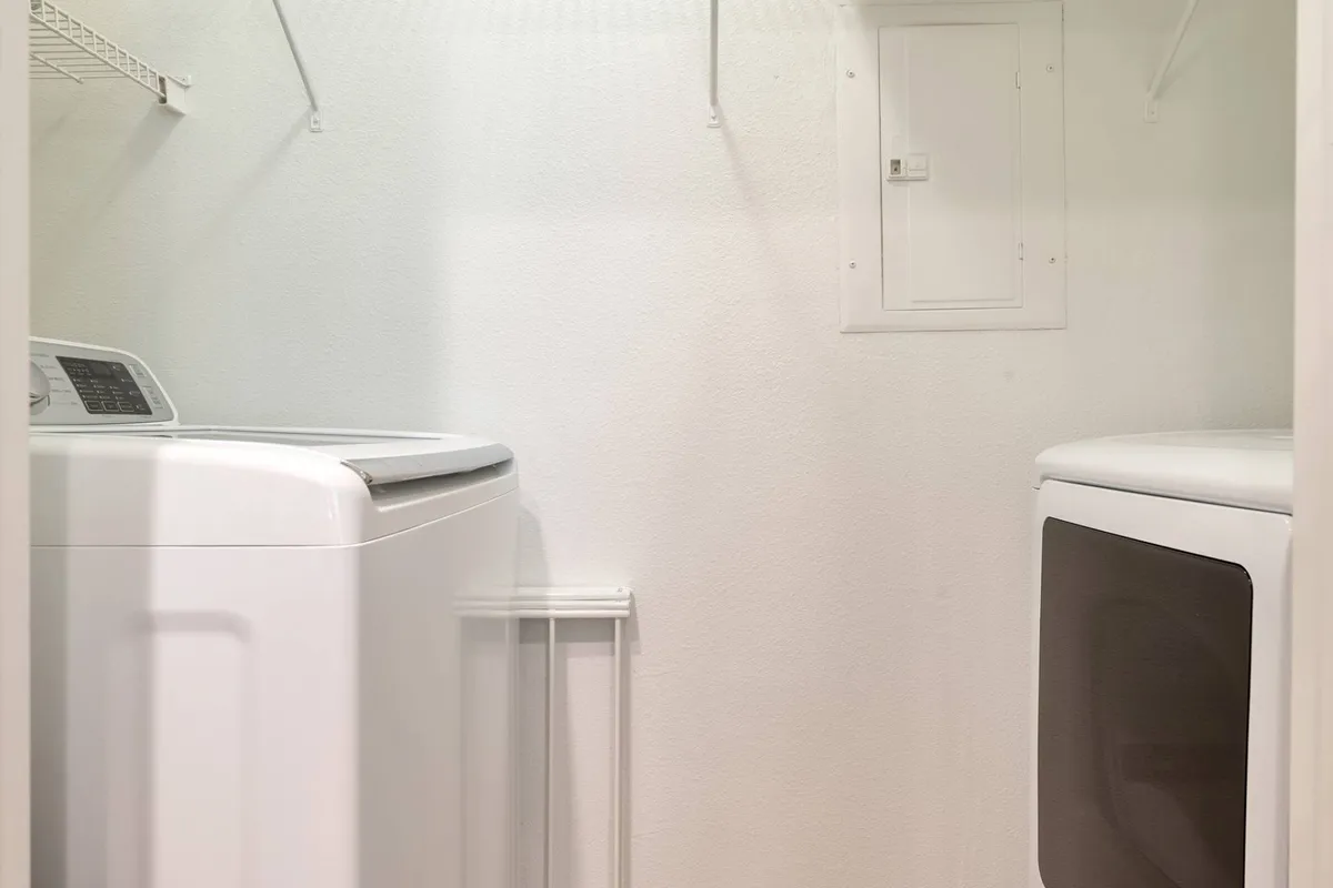 This image showcases a well-equipped laundry area featuring a washing machine, drying machine, and an organized shelving unit. The space feels practical yet serene, emphasizing convenience and order for extended stays.