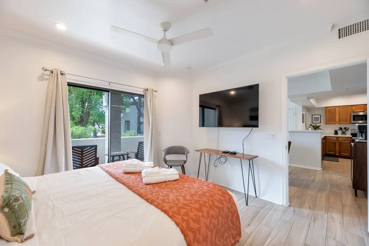 A comfortable bedroom set-up featuring a large bed with an orange throw, a wall-mounted TV perfectly positioned for movie nights, and a window framing a scenic view. The room is designed for both relaxation and entertainment, with plenty of natural light and modern decor.