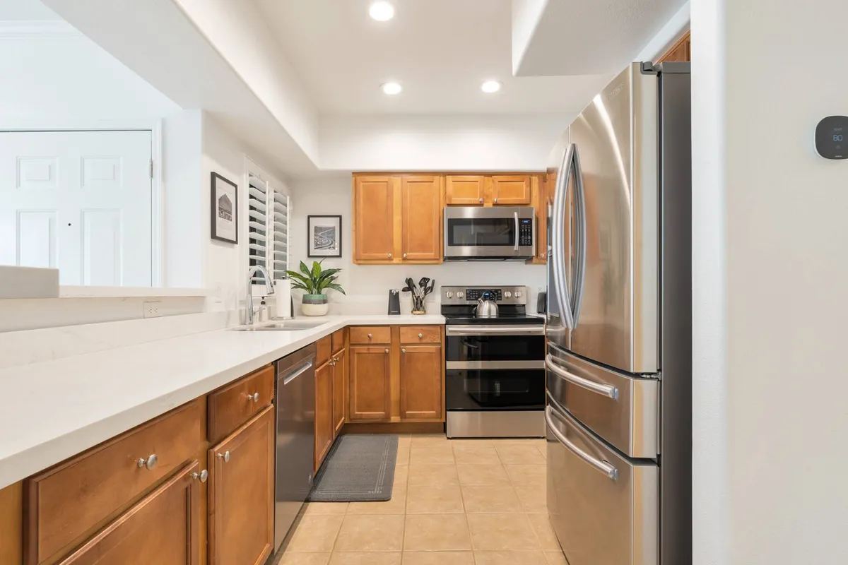 A warm and welcoming kitchen featuring stainless steel appliances, wooden cabinets, and a central kitchen island. The layout highlights ample space for meal preparation and gathering, with modern finishes that echo a homey, inviting atmosphere.
