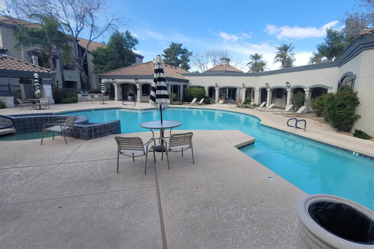 This exterior shot features a swimming pool framed by striped umbrellas and lounge chairs, creating a welcoming and lively environment for sunbathing, swimming, and socializing. The bright setting suggests fun social events and community engagement.
