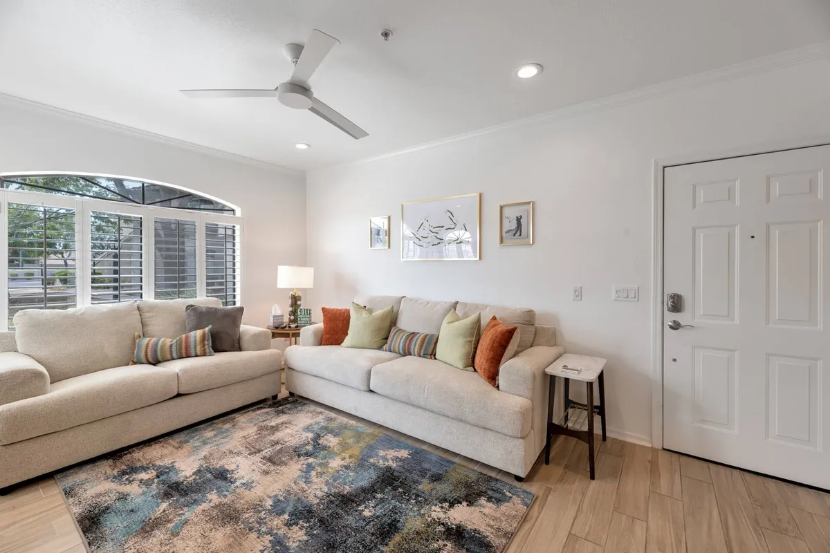 A view of the living room with multiple sofas arranged for both relaxation and socializing. The room is adorned with stylish artwork, a cozy rug, and a lamp, creating a comfortable, welcoming atmosphere ideal for gatherings or quiet reading.
