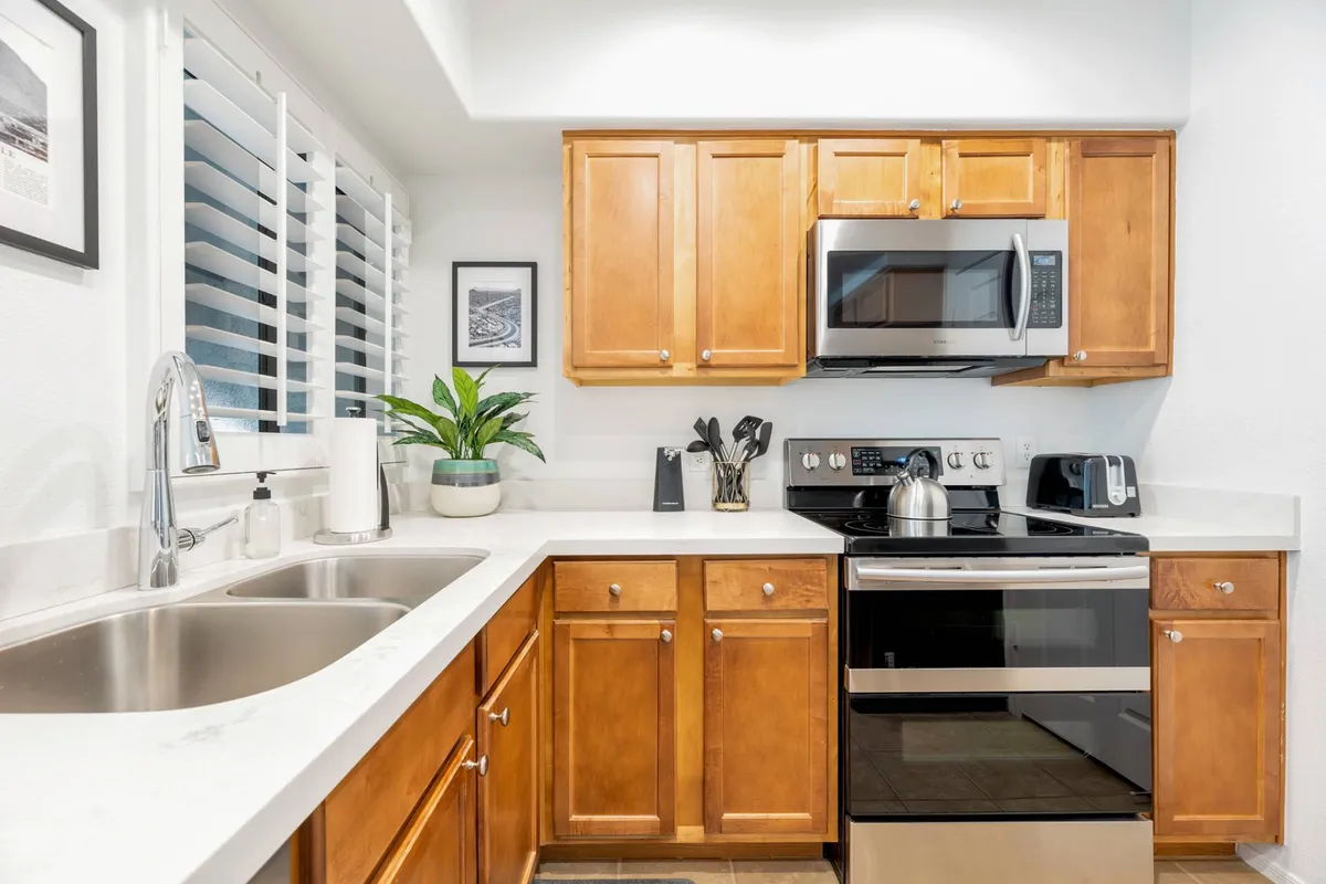 A cozy and functional kitchen corner with stainless steel appliances, wooden cabinets, a kitchen sink, potted plant, and plenty of countertop space. The arrangement suggests both efficient meal prep and a welcoming environment for family or friends to gather.