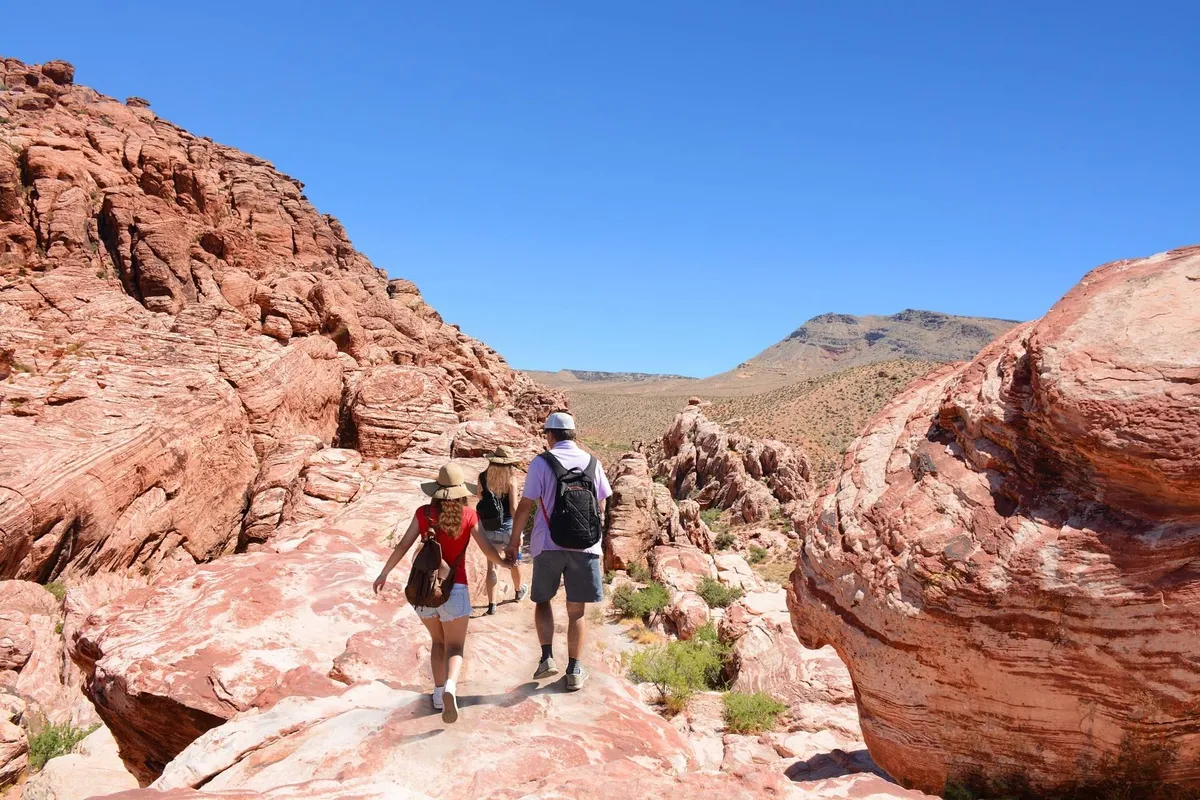 A dramatic landscape of red rock formations with hikers in the foreground, set against a rugged mountain backdrop. The scene encapsulates the spirit of outdoor exploration and discovery, making it ideal for families seeking adventure in nearby natural attractions.