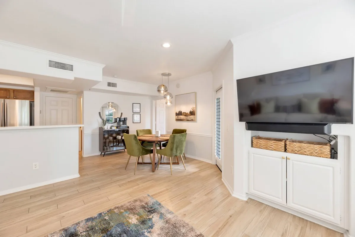 An interior view of a modern community living area, featuring a dining table with green chairs, a stylish TV unit, and elegant artwork on the wall. The space appears comfortable and designed for socializing, dining, or entertaining guests, embodying the 'gather with friends or family' amenity.