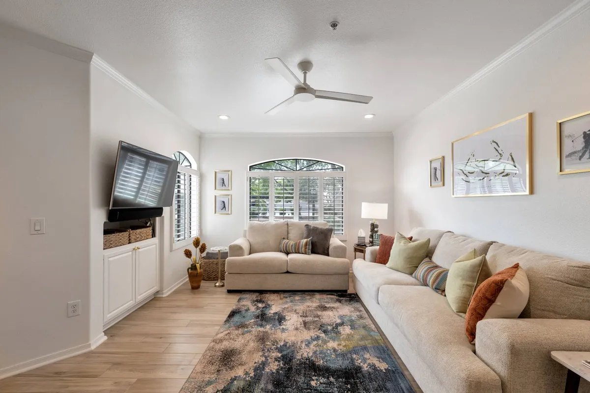 A cozy living area featuring a comfortable sofa and love seat positioned for both conversation and TV viewing. Large windows and sliding doors let in abundant natural light, and the space feels warm and inviting, perfect for relaxing after a day out.